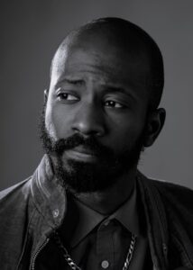 A close-up black and white headshot of a person with a beard